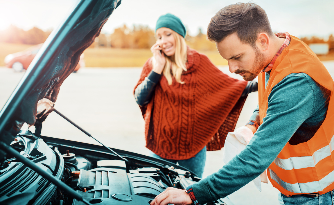 Woman talking on the phone while mechanic examines her car